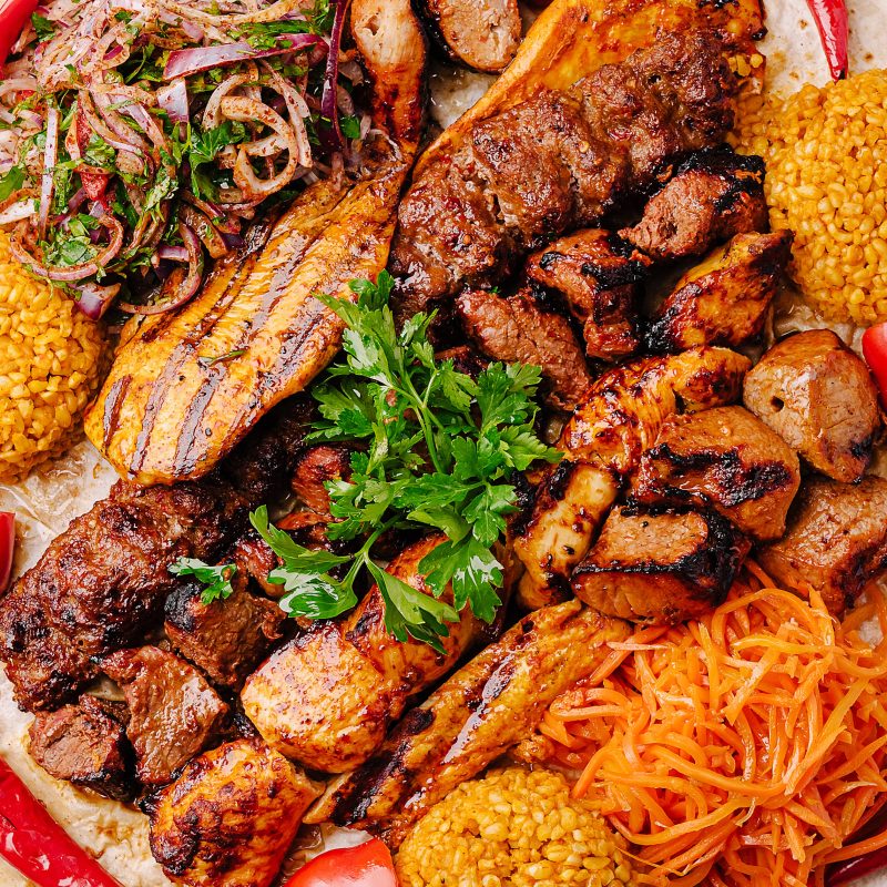 A vibrant mixed grill platter showcasing a variety of meats, aromatic sides, and fresh herbs. Perfectly grilled chicken, beef, and lamb are served with colorful rice, salad, and sauces.